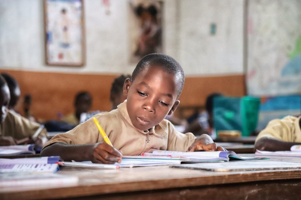pexels-photo-4587189 Young African boy focused on writing at his desk in a vibrant classroom setting.