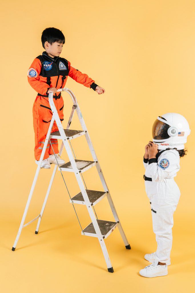 pexels-photo-5561469-5561469 Two kids in astronaut suits role-playing a space adventure against a yellow backdrop.